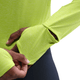 En person iført Nike Dri-FIT UV Long-Sleeve Crew-Neck Running Top, Dame, i Cyber/Htr/Reflective Silv viser tommelfingerhullet i ærmet ved at stikke tommelfingeren ind gennem åbningen. Baggrunden er hvid.