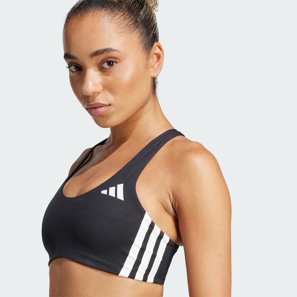 En kvinde i Adidas Adizero Medium Support Run Bra, Dame, Black - med hvide striber og logo - står på skrå mod en almindelig lys baggrund, klar til at løbe eller være aktiv.