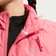 En person har en Nike Swift løbevest til damer i Sea Coral/Reflective Silver på over en sort top med lynlås, snøre med pink toggle og refleksstribe nær kraven. Venstre side af ansigtet og halsen er synlig.