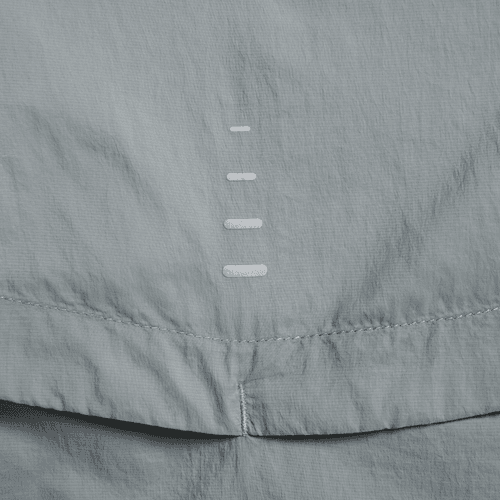 Et nærbillede af Nike Repel UV Running Jacket, Herre i Smoke Grey/Reflective Silv, viser lysegråt stof med en lodret søm og fem hvide stingmærker - hvilket understreger dens UV-beskyttende egenskaber.