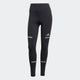 Adi365 Leggins til kvinder fra Adidas er sorte med høj linning, grå refleksstriber på lår og ben og et lille Adidas-logo på venstre lår. Vist mod en almindelig lys baggrund.