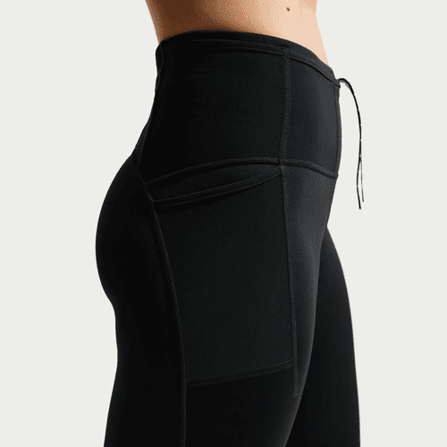 Nærbillede fra siden af en person iført Nike ACG High-Waisted 7/8 Running Tights (Dame) i Black/Summit White med synlige syninger, snøre i taljen og en sidelomme på en almindelig hvid baggrund.