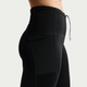 Nærbillede fra siden af en person iført Nike ACG High-Waisted 7/8 Running Tights (Dame) i Black/Summit White med synlige syninger, snøre i taljen og en sidelomme på en almindelig hvid baggrund.