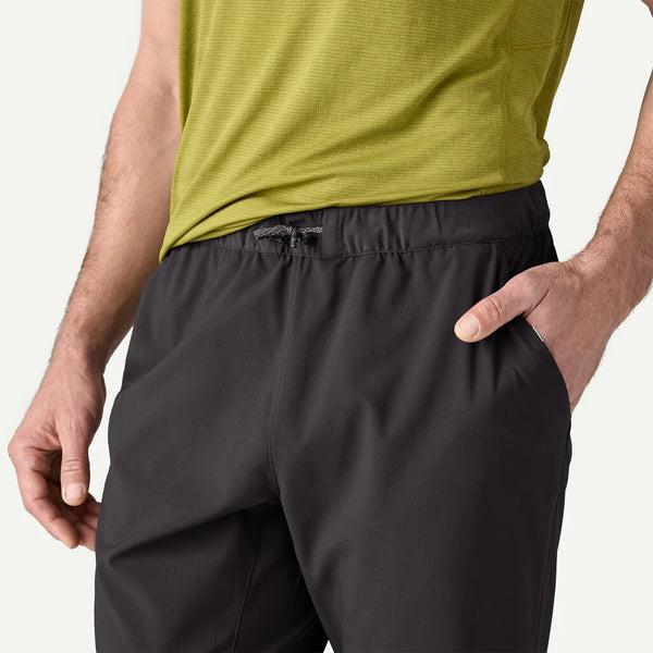 En person er iført en lysegrøn kortærmet skjorte og Patagonia Terrebonne Joggers, Herre, Black med den ene hånd i lommen. Billedet fremhæver taljen og den øverste del af låret på disse Patagonia-joggers.