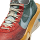 Et nærbillede af Nike Alphafly Next% 3 Prm (Herre) i Multi-Color/Clear-Starfish-Aloe Verde viser hvide snørebånd, en lyseblå swoosh, ZoomX-skum og en blå globusgrafik med tekst på siden.