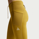 En person er iført Nike ACG 7/8 Running Tights til kvinder i Peat Moss/Ironstone/Summit White med synlige sømme, en sidelomme og et lille ACG-logo på låret. Kun underkroppen og overbenene er vist mod en almindelig baggrund.