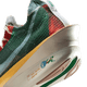 Nærbillede af hælen og sålen på Nike Alphafly Next% 3 Prm Herre løbesko i Multi-Color/Clear-Starfish-Aloe Verde med en flerfarvet mesh-overdel, gul ZoomX-skum-mellemsål og "Nike Road Racing" med en globusgrafik på den hvide, buede hæl.