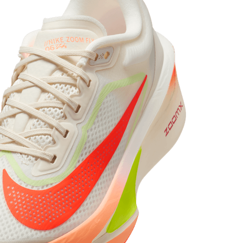 Et nærbillede af Nike Zoom Fly 6 Dame i Pale Ivory/Hyper Crimson med orange swoosh, neongule og orange detaljer, hvide snørebånd og "ZOOMX" trykt på den tykke sål.