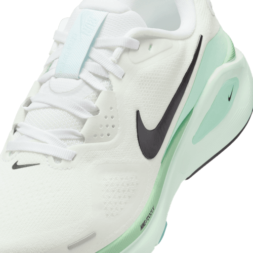 Et nærbillede af Nike Structure 26 Dame i White/Black-Barely Green-Mint Foam viser en sort Swoosh, lysegrønne detaljer på sålen, en lyseblå label på tungen, hvide snørebånd og en overdel i mesh, der giver stabilitet.