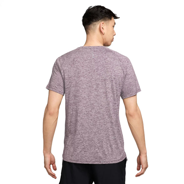 En mand ses bagfra i en Nike Stride SS Running Top til mænd, Lt Violet Ore/Reflective Silver, og sorte shorts, der fremhæver denne fugttransporterende træningstrøje mod en almindelig hvid baggrund.