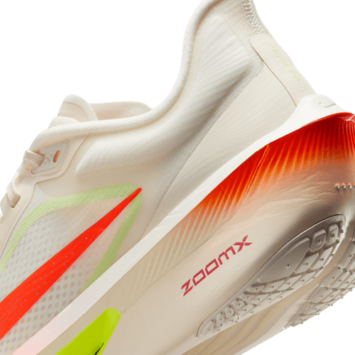 Et nærbillede af hælen og sålen på Nike Zoom Fly 6, Dame, Pale Ivory/Hyper Crimson løbesko viser røde, neongrønne og orange accenter. ZOOMX-logoet vises på slidbanen og fremhæver dens kulfiberplade for forbedret ydeevne.