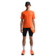 En person ser fremad i en Nike ACG Dfadv Solar Chase Ss tee (Safety Orange/Summit White), sorte shorts, hvide sokker, orange sko og en sort kasket med en orange vandflaske i hånden. Baggrunden er almindelig hvid.