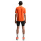En mand kigger væk fra kameraet iført Nike ACG Dfadv Solar Chase Ss træningstop i Safety Orange/Summit White, parret med sorte shorts, hvide sokker, orange sneakers og en sort kasket. Baggrunden er helt hvid.