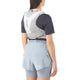 En person med langt mørkt hår, i sort skjorte, lyseblå løbeshorts og en Salomon ADV Skin 5 Unisex vest i Alloy/Gray Violet/Spellbo, står med ryggen til kameraet - klar til terrænløb.
