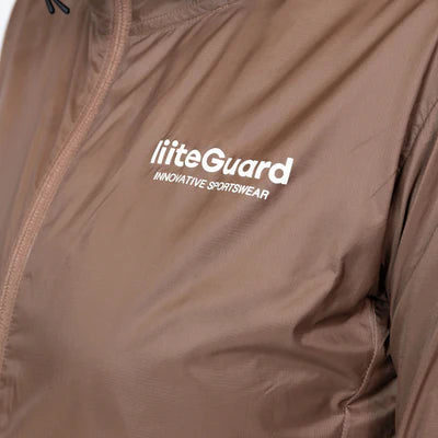 Nærbillede af Liiteguard Aero-Tech Windbreaker, Dame, i Cocoa Brown. Har et hvidt broderet "liiteGuard INNOVATIVE SPORTSWEAR"-logo på venstre bryst. Fremstillet af let, skinnende, åndbart, vand- og vindafvisende materiale.