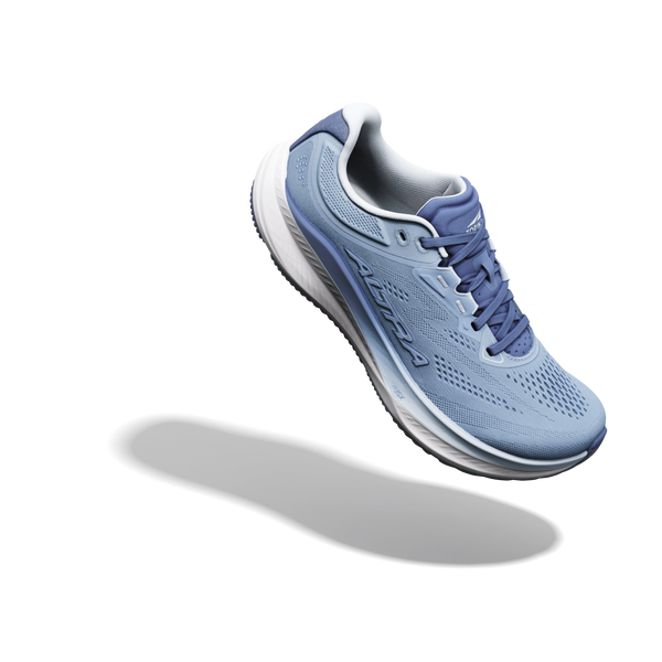 En Altra Torin 9 Dame-løbesko i farvekombinationen Windward Blue/White/Dark Denim vises svævende over en hvid baggrund, hvor den kaster en skygge under sig. Skoen har Zero Drop, en hvid mellemsål, en ydersål i mørk denim og blå snørebånd.