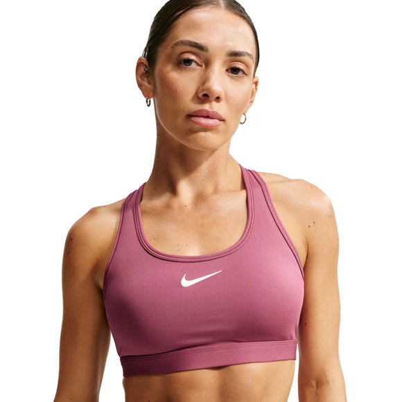 En person, der bærer Nike Padded Sports Bra, Dame i farven Pink Smoke/White, står foran en ensfarvet baggrund og ser direkte ind i kameraet. Håret er sat op, og personen bærer små ringøreringe.