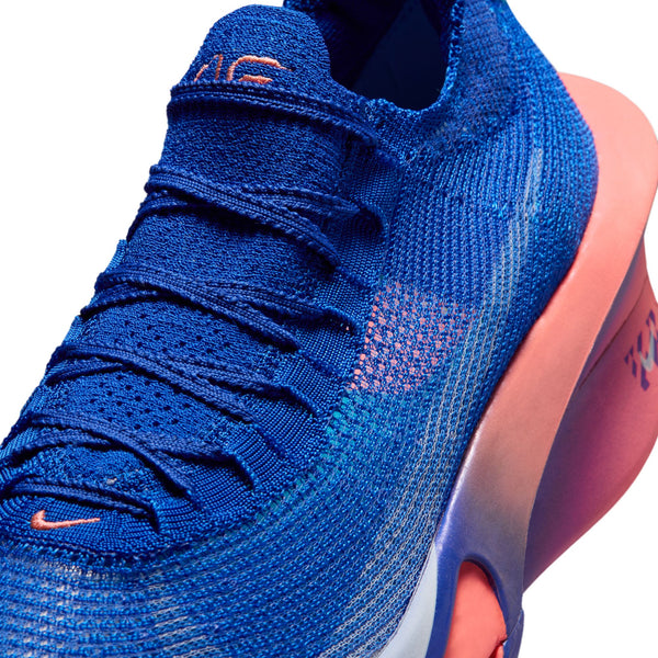 Nærbillede af Nike Alphafly 3, Herre i Racer Blue/White-Atomic Pink, en sportslig sneaker med strikket overdel, orange detaljer og en tyk sål, der skifter farve fra lyserød til lilla. Den er designet som maratonsko og løbesko til mænd og har detaljeret snøring samt et lille Nike-logo tæt på tåen.