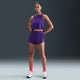 En person står med ansigtet fremad og armene ned langs siden iført Nike Aeroswift 3" løbeshorts til kvinder i Court Purple/White, en matchende ærmeløs sportstop, røde sokker og hvide sneakers på en almindelig mørk baggrund.