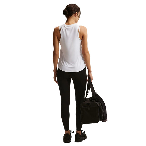 En kvinde kigger væk mod en almindelig hvid baggrund iført Nike Nk One Classic Df Tank (Dame, White/Black), sorte leggings og sko. Hun holder en sort sportstaske i venstre hånd og har håret bundet tilbage i en lav knold.