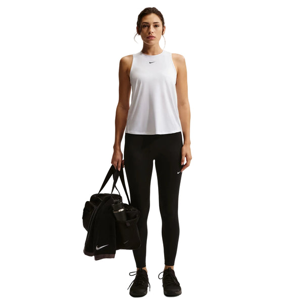 En kvinde kigger fremad i en Nike Nk One Classic Df Tank, Dame, White/Black og sorte leggings, mens hun holder en sort sportstaske og en vandflaske i venstre hånd. Hun har sorte sportssko på, alt sammen på en almindelig hvid baggrund.