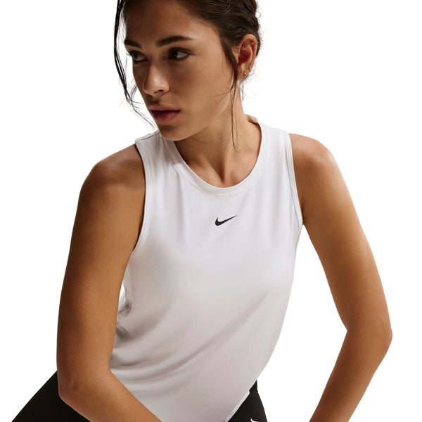 En kvinde med mørkt hår, der er trukket tilbage, bærer Nike Nk One Classic Df Tank til kvinder i hvid/sort med et lille sort logo på brystet, mens hun står på en almindelig hvid baggrund.