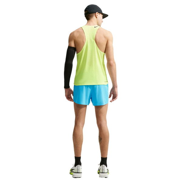 En mand står med ryggen til og er iført en sort kasket, en ærmeløs gul sportstrøje, Nike AeroSwift 4" løbeshorts med indvendig underbuks i farven Lt Current Blue/Black, hvide sneakers, sorte sokker og en sort kompressionsærme på højre arm.