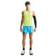 En person står med ansigtet vendt fremad iført en neongul tanktop, Nike AeroSwift 4" løbeshorts med indvendig underbuks i farven Lt Current Blue/Black, en sort armvarm, en sort kasket og sort-hvide løbesko; Nike-logoer er synlige.