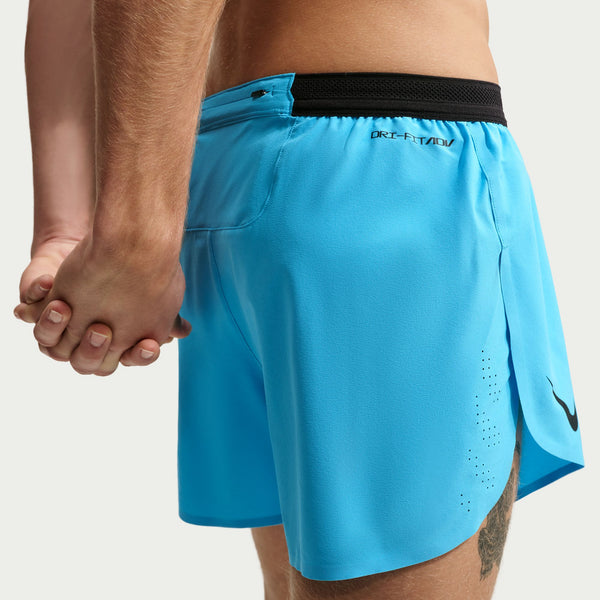 Nærbillede af to personer, der holder hinanden i hånden. Den ene har Nike AeroSwift 4" løbeshorts til mænd med underbukser i farven Lt Current Blue/Black på, med sort linning og logo; disse shorts byder på både komfort og stil. En del af deres ben og hænder er synlige.