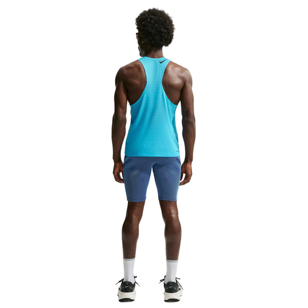 En person står med ryggen til og har Nike AeroSwift Running Half Tights til mænd i farverne Baltic Blue/Black/Old Royal/Black på, kombineret med en matchende, lyseblå ærmeløs sportstrøje, hvide sokker og sorte sportssko. Looket forener sporty komfort med den strømlinede pasform af disse svedtransporterende tights på en ensfarvet hvid baggrund.