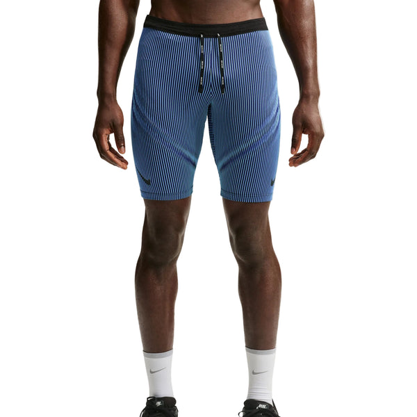 Der vises et billede af en person fra livet og ned, iført Nike AeroSwift Running Half Tights til mænd i farverne Baltic Blue/Black/Old Royal/Black, som er trukket uden på et par blå og hvide, lodret stribede sportsshorts med sort linning og snøre, kombineret med hvide sokker og sorte sportssko.