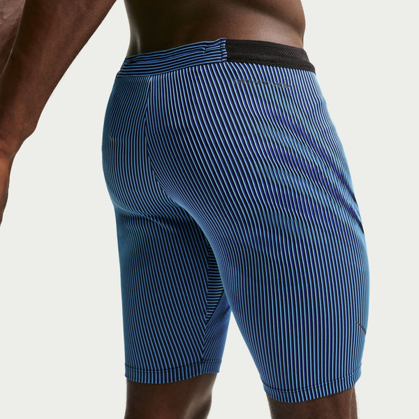 Der vises et billede af en person fra livet og ned, iført Nike AeroSwift Running Half Tights til mænd i farvekombinationen Baltic Blue/Black/Old Royal/Black med sort linning, stående foran en ensfarvet lys baggrund.