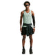 En person står med ansigtet fremad og er iført en grøn Nike AeroSwift Running Singlet, Herre, Steam/Black med Dri-FIT ADV-teknologi, sorte løbeshorts og sneakers, solbriller, et sort ærme og en sort jakke, der er bundet i taljen.
