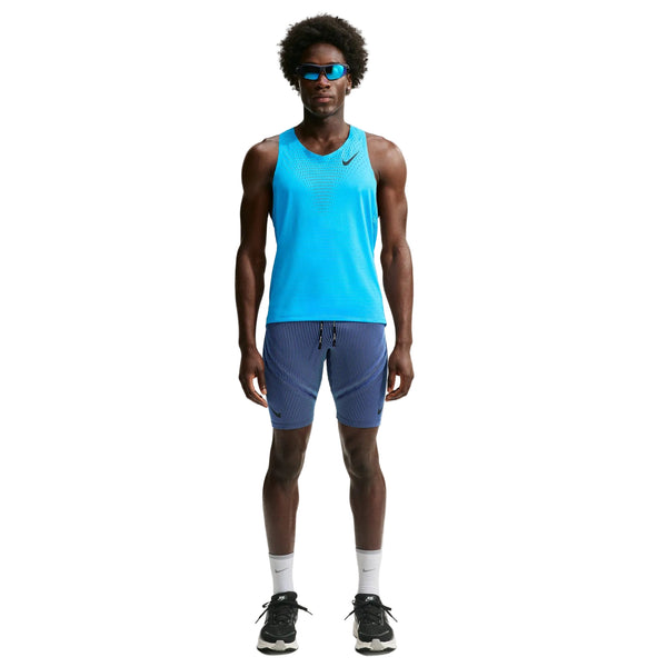 En mand står med ansigtet vendt fremad iført en Nike AeroSwift løbetrøje til mænd i farven Lt Current Blue/Black, blå shorts, hvide strømper, sorte løbesko og blå solbriller foran en ensfarvet hvid baggrund.