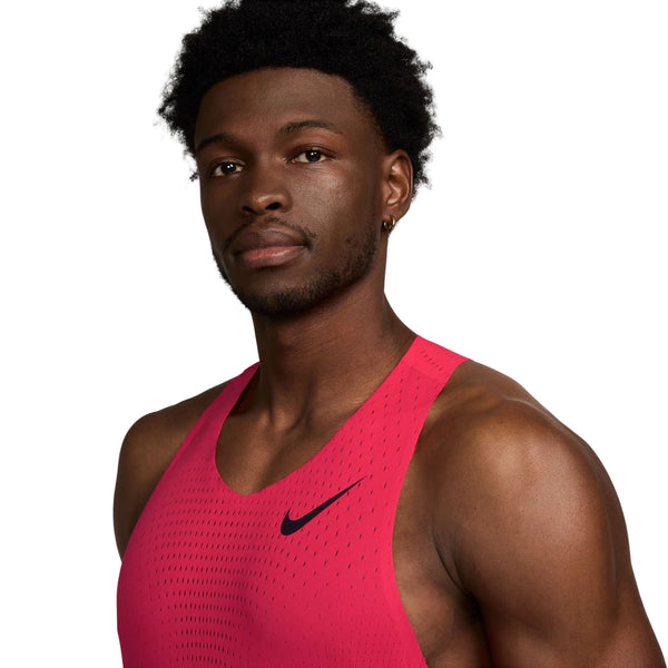 En mand iført en ærmeløs Nike AeroSwift løbesinglet til herre i farvekombinationen Fusion Red/Black poserer foran en hvid baggrund og kigger let til siden. Denne løbesinglet til herre er designet med avanceret Dri-FIT-teknologi, der hjælper med at holde dig kølig og tør under din træning.