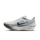 Et billede set fra siden af Nike Zoom Fly 6, Herre i farvekombinationen Pure Platinum/Dark Obsidian-Grey Fog viser en grå og hvid sko med et sort Swoosh-logo, en gennemsigtig overdel, tekst på mellemsålen, grønne detaljer på hælen og en tyk, buet ZoomX-skum-sål.