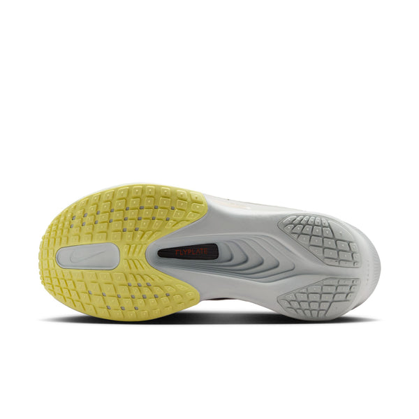 Billedet viser sålen på Nike Zoom Fly 6 Dame i farvekombinationen Bleached Lilac/Purple Dynasty-Volt Tint, med en gul ydersål på venstre sko, en grå ydersål på højre sko og teksten »FLYPLATE« på en sort stribe over det bløde ZoomX-skum.