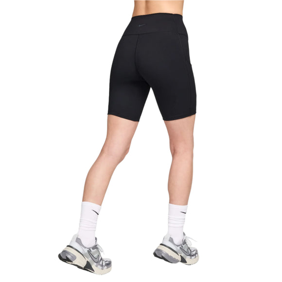 En person står med spredte ben og ryggen til kameraet mod en hvid baggrund iført Nike One High-Waisted 8" Biker Shorts With Pockets i sort/sort, hvide Nike-sokker og grå og hvide sneakers.