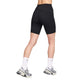 En person står med spredte ben og ryggen til kameraet mod en hvid baggrund iført Nike One High-Waisted 8" Biker Shorts With Pockets i sort/sort, hvide Nike-sokker og grå og hvide sneakers.