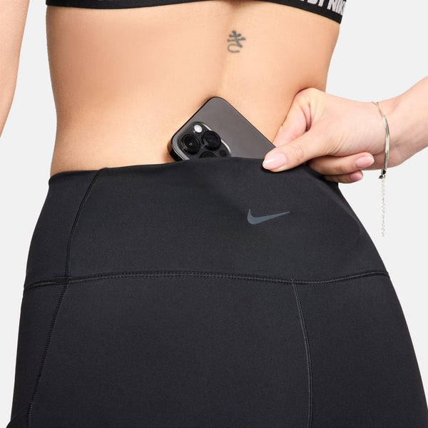 En person stikker en sort smartphone ned i lommen på Nikes One High-Waisted 8" Biker Shorts With Pockets, Dame, Black/Black, og afslører en lille tatovering på lænden og en del af en sports-bh.