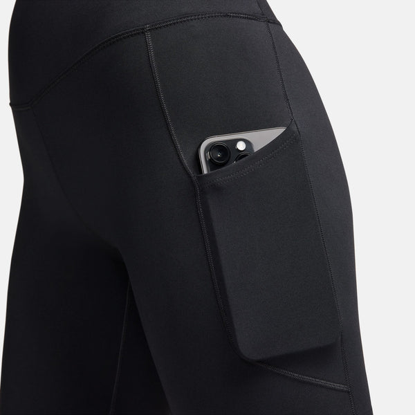 Et nærbillede viser en person iført Nikes One High-Waisted 8" Biker Shorts With Pockets i sort, med en smartphone delvist synlig i lårlommen mod en almindelig hvid baggrund.