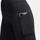 Et nærbillede viser en person iført Nikes One High-Waisted 8" Biker Shorts With Pockets i sort, med en smartphone delvist synlig i lårlommen mod en almindelig hvid baggrund.