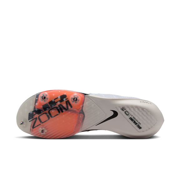 Undersiden af Nike Victory 2 Proto (Unisex, White/Black-Total Orange) løbesko har metalspikes, en gennemsigtig sål med orange accenter, sort Zoom-branding og Nike-logo, teknisk tekst og antydninger af kulfibersål nær hælen.