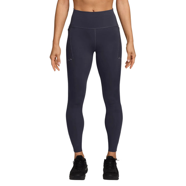 En person står med ansigtet fremad foran en hvid baggrund og har Nike Swift High-Waisted 7/8 løbetights med lommer til kvinder i farven Gridiron/Reflective Silv på. Løbetightsene har synlige sømme, refleksdetaljer og praktiske sidelommer. Overkroppen og fodtøjet er ikke vist.