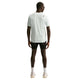 En mand ser væk, iført en Nike Nk Dfadv Aroswft Ss Top, Herre i Summit White/Black, parret med sorte shorts, hvide sokker og sneakers, plus solbriller, der står mod en almindelig hvid baggrund.