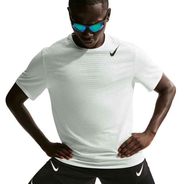 En mand i Nike Nk Dfadv Aroswft Ss Top, Herre, Summit White/Black og sorte Nike-shorts poserer med spejlende solbriller og hænderne på hofterne mod en hvid baggrund for at fremhæve den nyeste løbekollektion.
