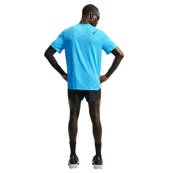 En mand står med ryggen til og er iført en Nike AeroSwift kortærmet løbetrøje til mænd i farven Lt Current Blue/Black, sorte løbeshorts, sorte kompressionsærmer, sorte sokker, løbesko og solbriller foran en hvid baggrund.