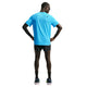 En mand står med ryggen til og er iført en Nike AeroSwift kortærmet løbetrøje til mænd i farven Lt Current Blue/Black, sorte løbeshorts, sorte kompressionsærmer, sorte sokker, løbesko og solbriller foran en hvid baggrund.