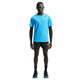 En person står med ansigtet vendt fremad iført en Nike AeroSwift løbetrøje med korte ærmer i farven Lt Current Blue/Black, sorte Nike-shorts, sorte sokker, løbesko, solbriller og en armvarmere foran en ensfarvet hvid baggrund.