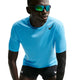 En mand iført en lyseblå Nike AeroSwift løbetrøje med korte ærmer (Herre, Lt Current Blue/Black), sorte kompressionsshorts, sort armbeskytter og reflekterende solbriller læner sig fremad foran en hvid baggrund.